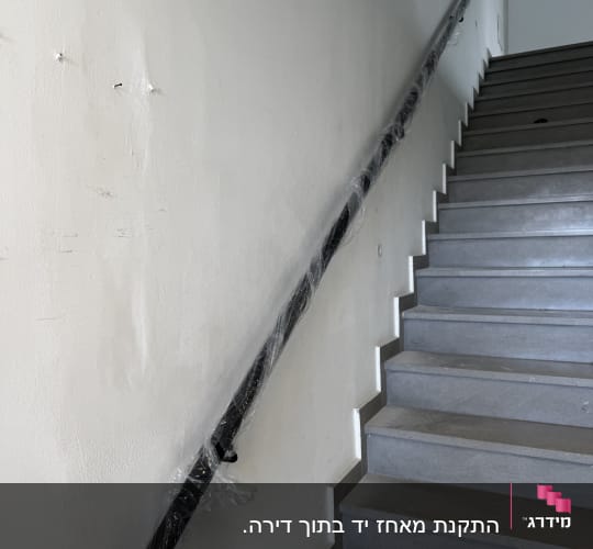 מעקה שחור עטוף בניילון לאורך מדרגות אפורות
